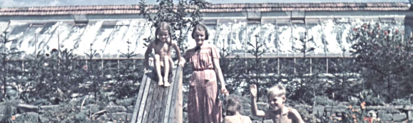 Die Mutter Hedwig Höß steht mit ihren Kindern in einem Garten an einer Wasserrutsche. Der Garten ist die Villa Höß im KZ Auschwitz